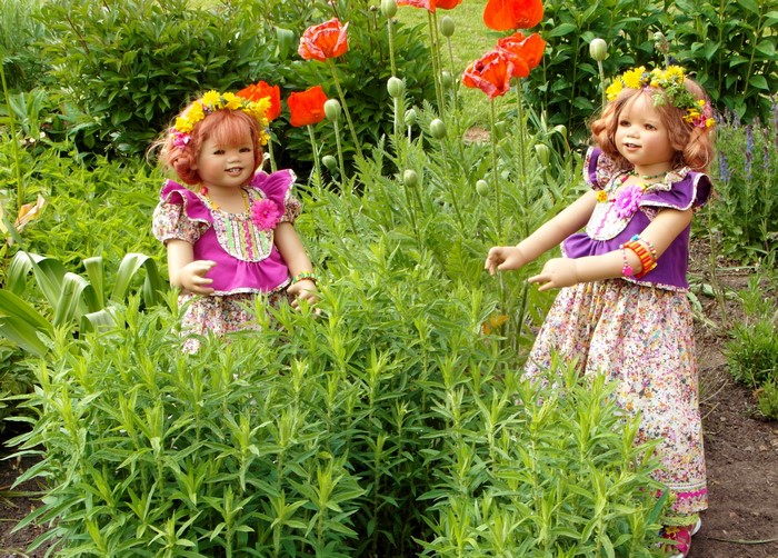 Two dolls dressed as little girls in a garden with poppies