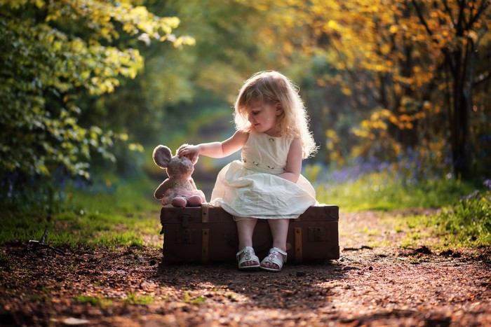 Little girl sitting on a suitcase with a toy