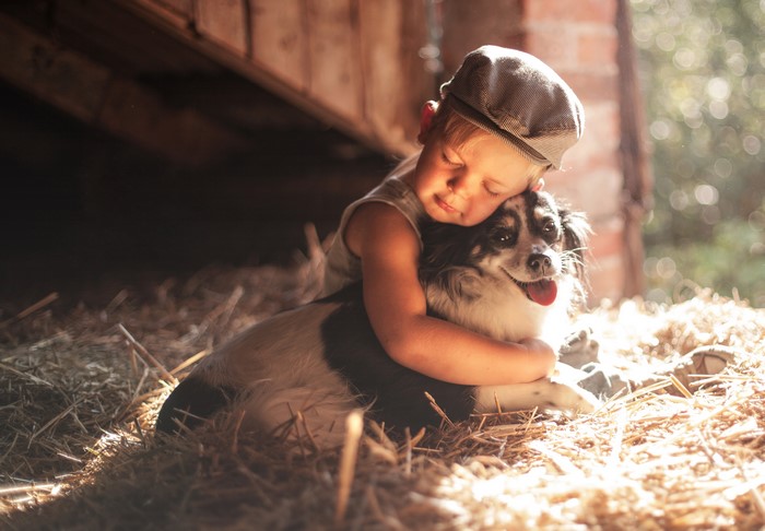 Boy hugging a dog in hay
