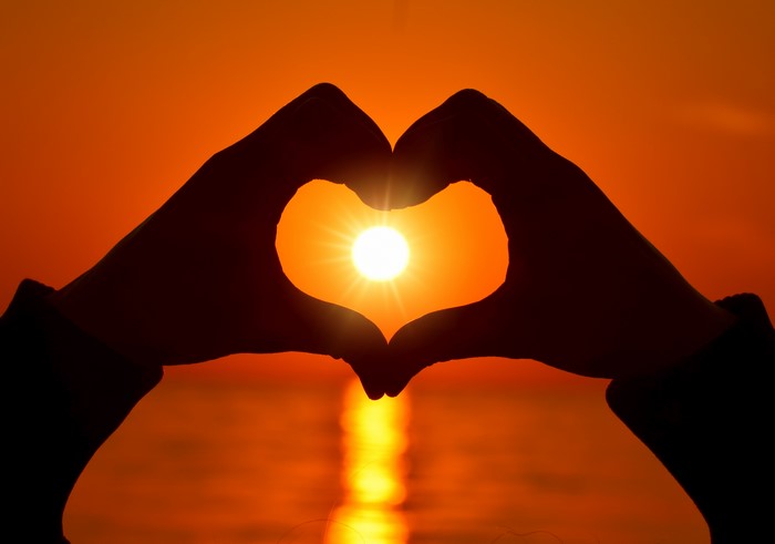 Hands forming a heart shape around the sun at sunset