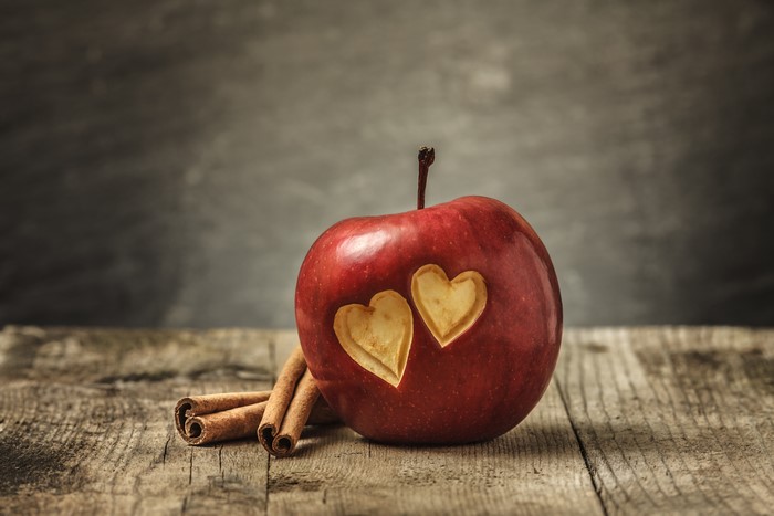 Red apple with carved hearts and cinnamon sticks