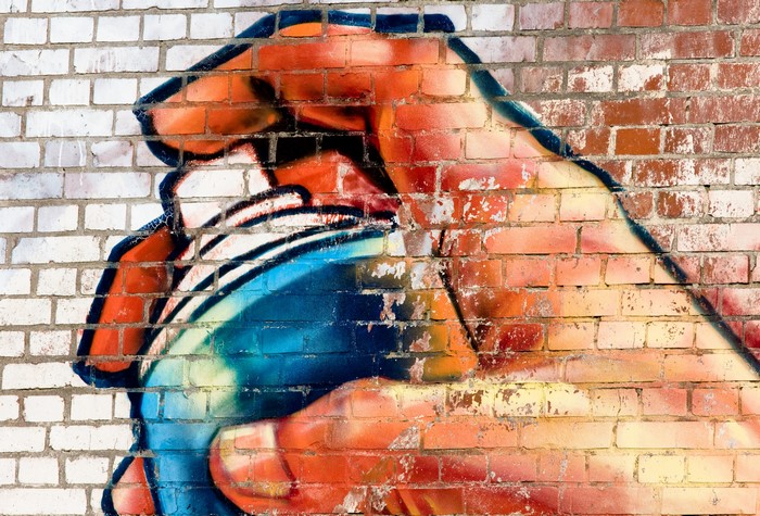 Graffiti of a hand holding a spray can on a brick wall