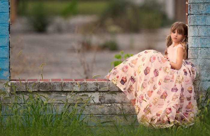 Young girl in cupcake dress sitting by brick wall