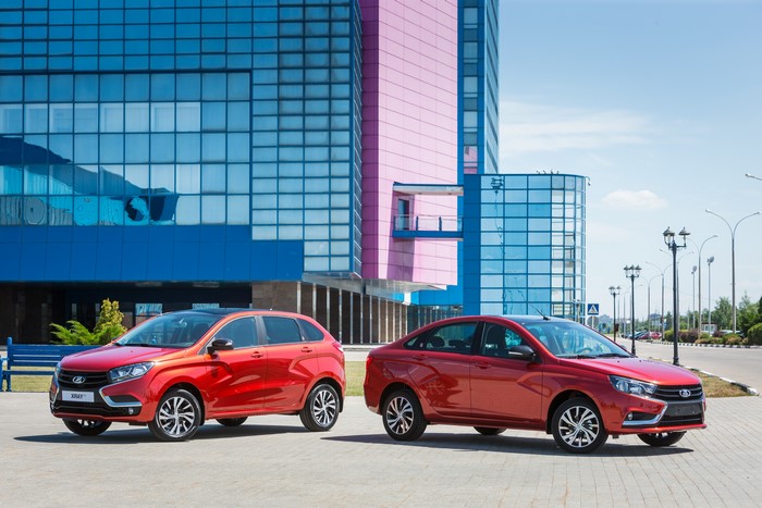 Two red Lada cars, Vesta and X-ray, in front of a modern building