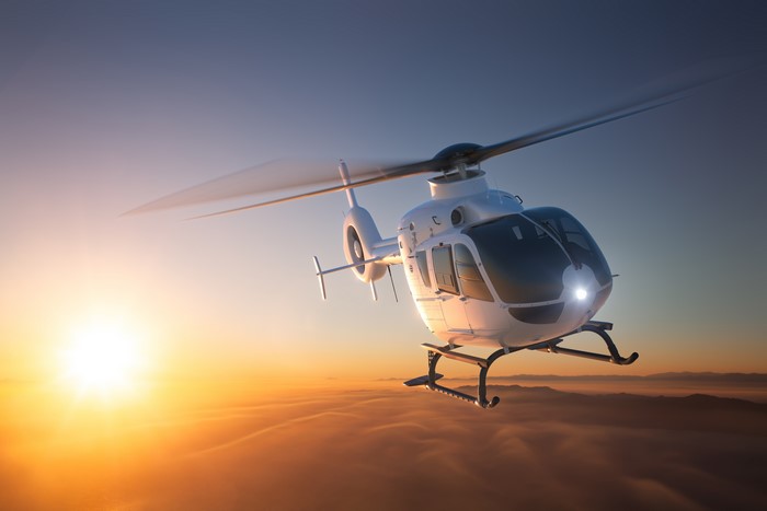Eurocopter EC 135 helicopter flying over clouds at sunset