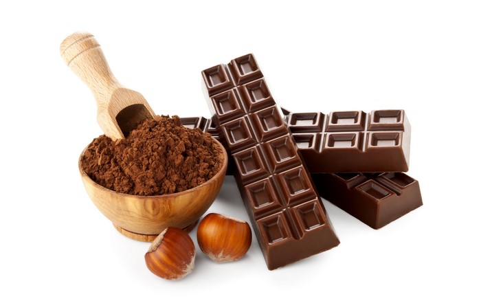 Chocolate bars, cocoa powder, and hazelnuts on white background