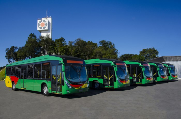 Green buses lined up in front of a tower