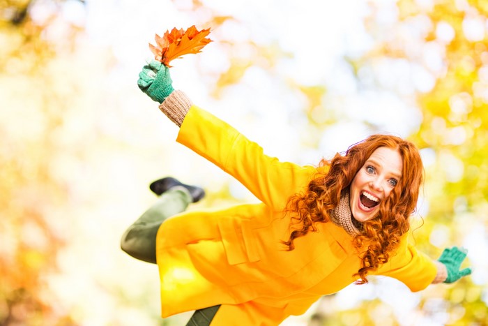 Joyful redhead girl in autumn park holding leaves