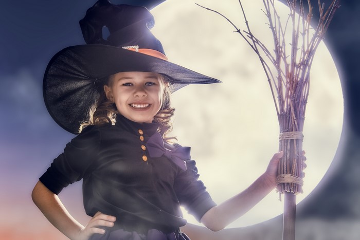 Girl in witch costume holding a broomstick in front of the moon