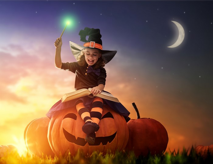 Girl in Witch Costume with Magic Wand on Pumpkin