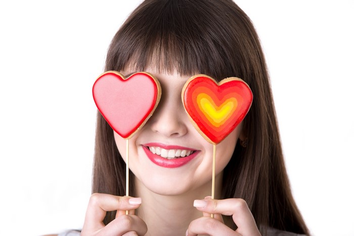 Woman holding heart cookies over eyes