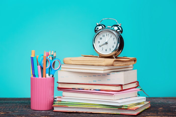 Alarm clock on stack of books with school supplies