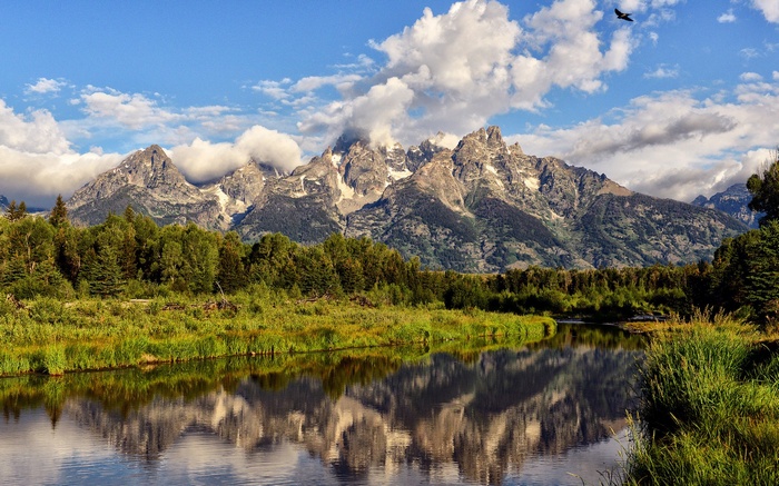 Mountains reflected in a river with trees and clouds