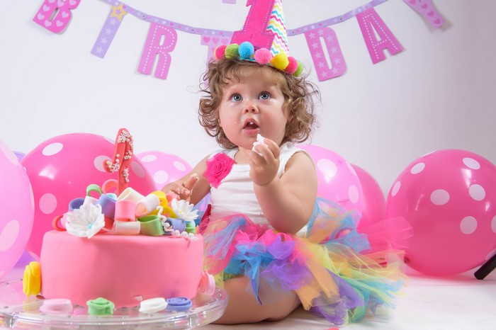 Baby girl's first birthday party with cake and balloons