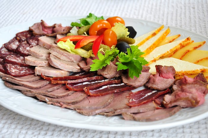Assortment of sliced meats and cheeses on a white plate