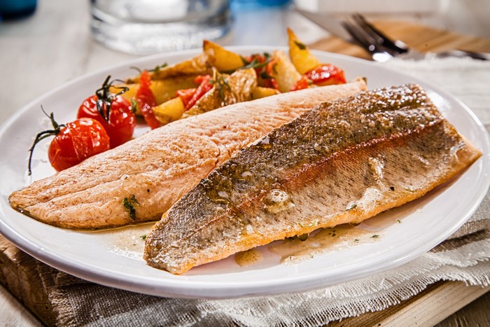 Two fish fillets with roasted potatoes and cherry tomatoes on a plate