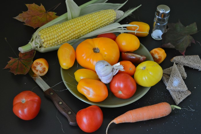 Corn, tomatoes, garlic, carrot, bread, and salt on a dark surface