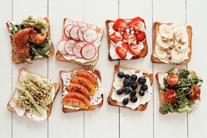 Eight open-faced sandwiches with various toppings on wooden planks