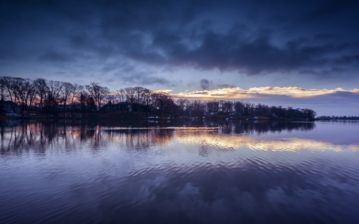 Lake with trees and cloudy sky at dusk