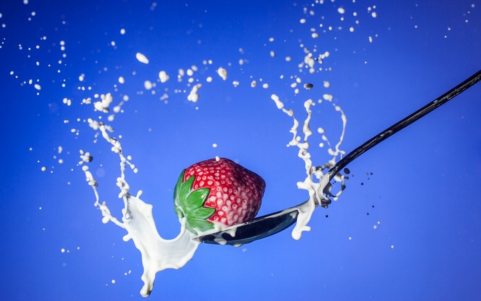 Strawberry splashing into milk on a spoon