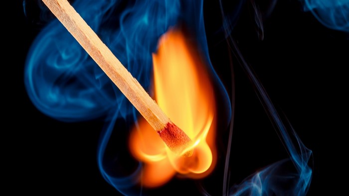 Close-up of a burning match with blue smoke