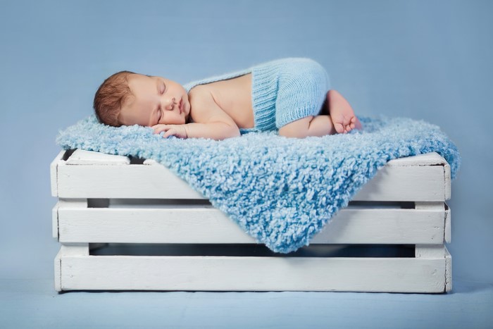 Infant sleeping on a blue blanket on a wooden crate