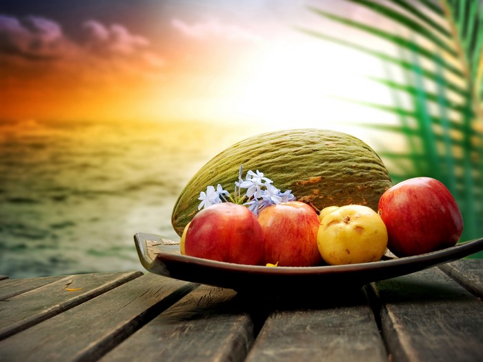 Fruit bowl with apples and melon on a wooden table at sunset