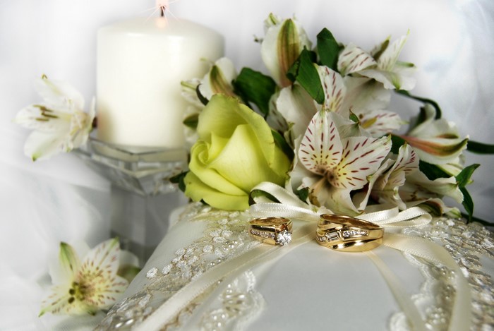 Wedding rings on a pillow with flowers and a candle