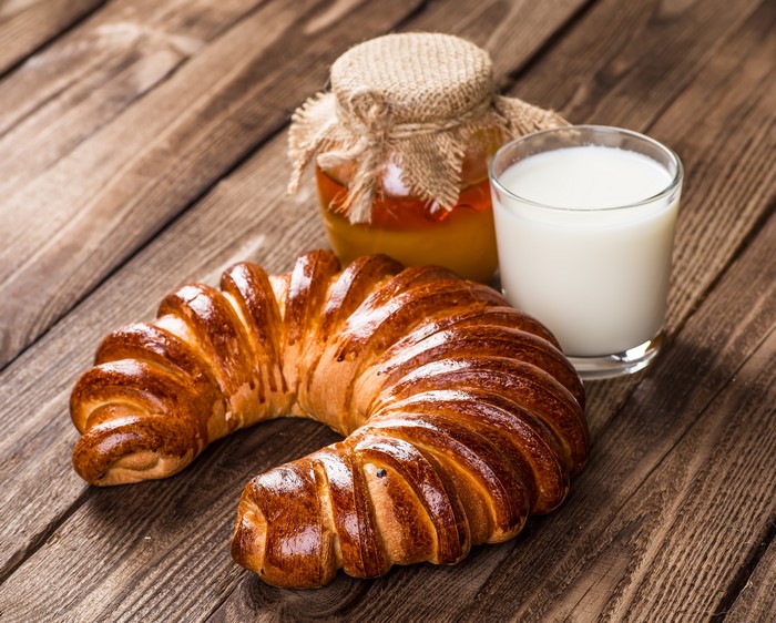 Croissant with honey and milk on wood