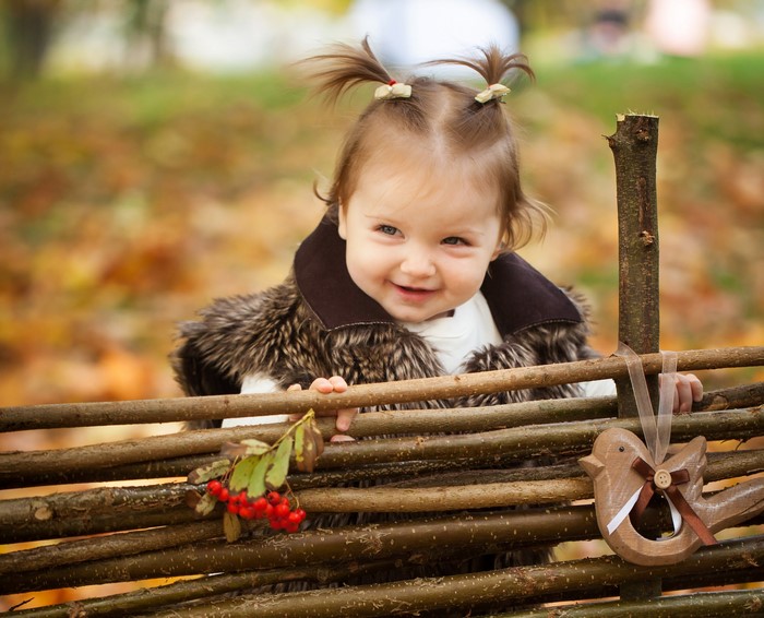 Baby girl in fur coat behind a wooden fence