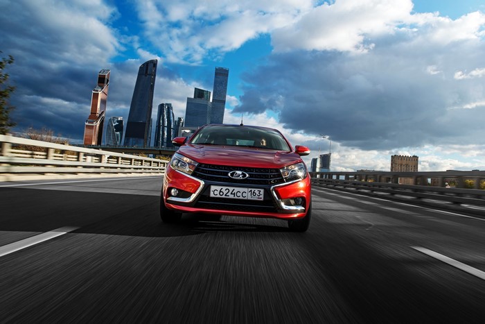 Red Lada Vesta driving on a highway with skyscrapers