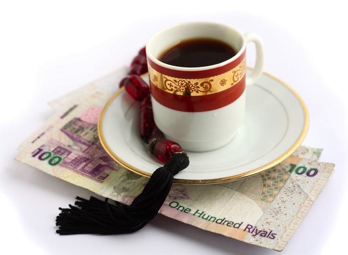Coffee cup on Qatari Riyal banknotes with prayer beads