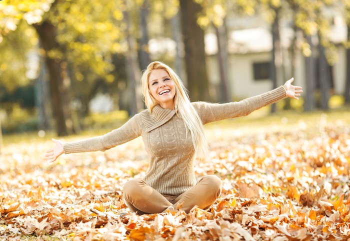 Blonde woman sitting in autumn foliage wearing a sweater