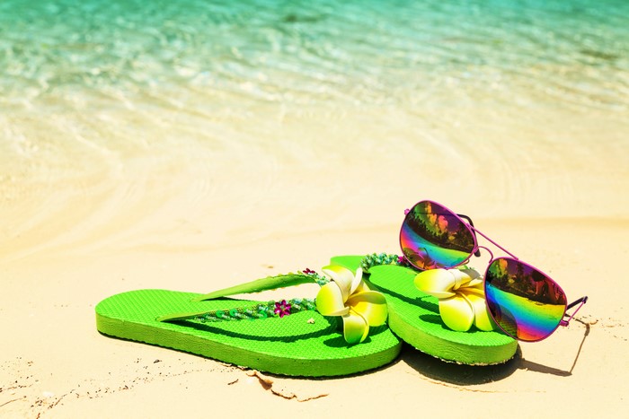 Green flip-flops with flowers and sunglasses on a beach