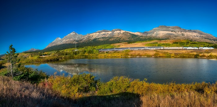 Train passing by a lake with mountains in Glacier National Park