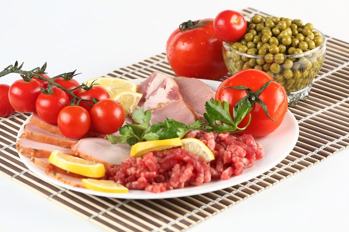 Meat products, tomatoes, green peas, and lemon on a plate