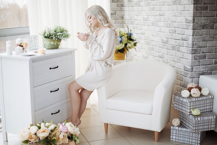 Blonde girl holding a cup near a dresser