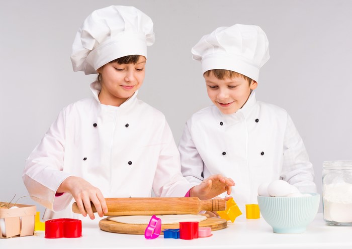 Two young chefs rolling dough with cookie cutters