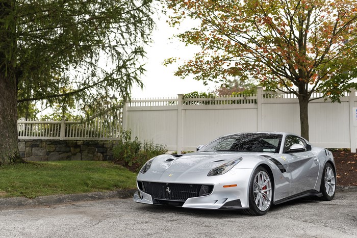 Grey Ferrari F12tdf parked near a white fence