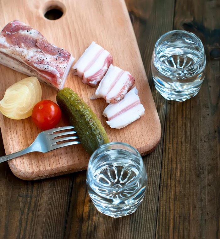 Salo, pickles, tomato, onion, and vodka shots on a cutting board