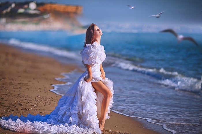 Woman in white dress on a beach with seagulls