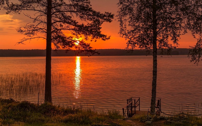 Sunset over a calm lake with trees and a dock