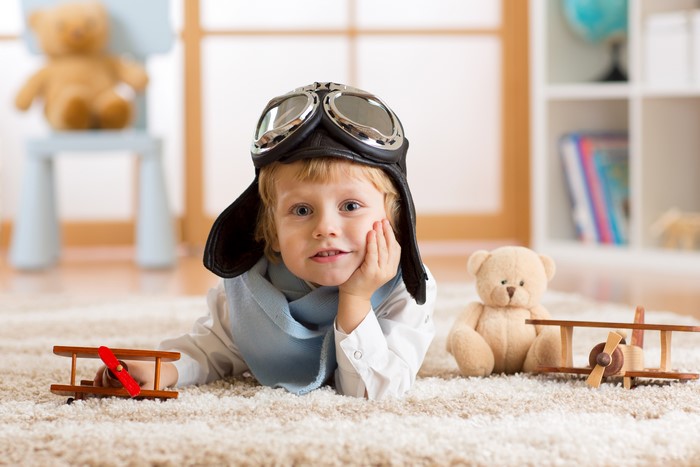 Boy in pilot hat with toy airplanes and teddy bear