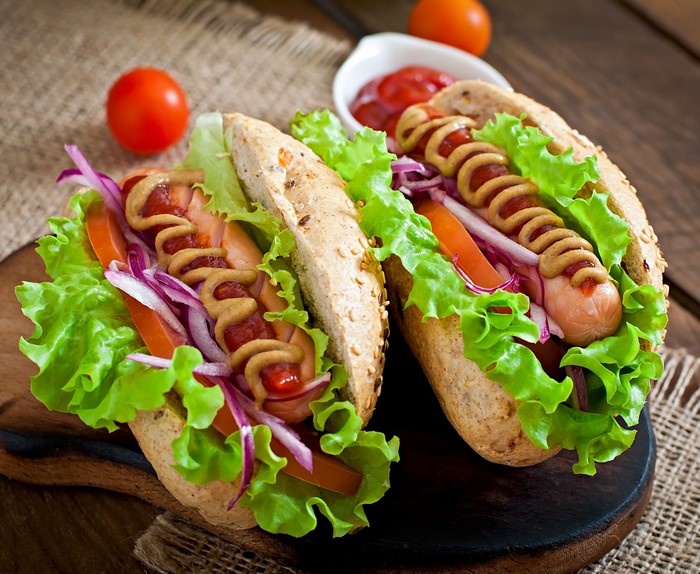 Two hot dogs with toppings on a wooden board