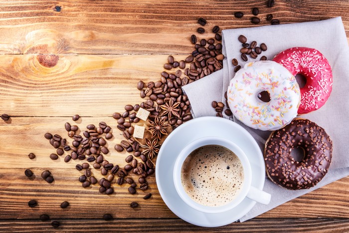 Coffee cup with donuts and coffee beans on wooden table
