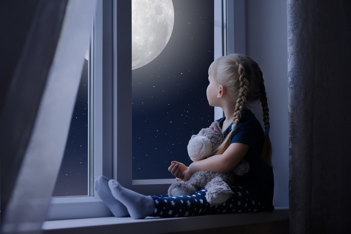 Little girl sitting by the window at night