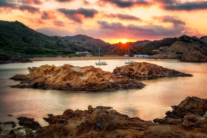 Sunset over the bay with sailboats and rocky coast in Ciutadella de Menorca