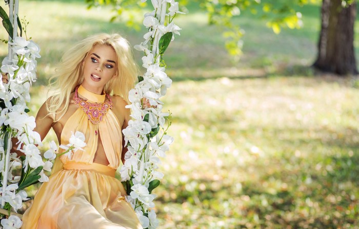 Blonde girl in a dress on a swing with flowers