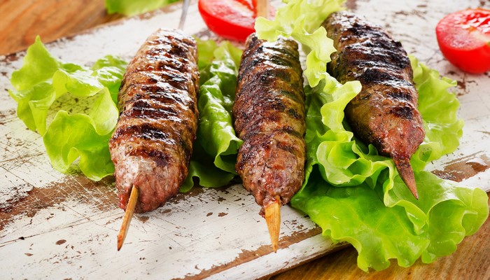 Three grilled kebabs on lettuce with tomatoes