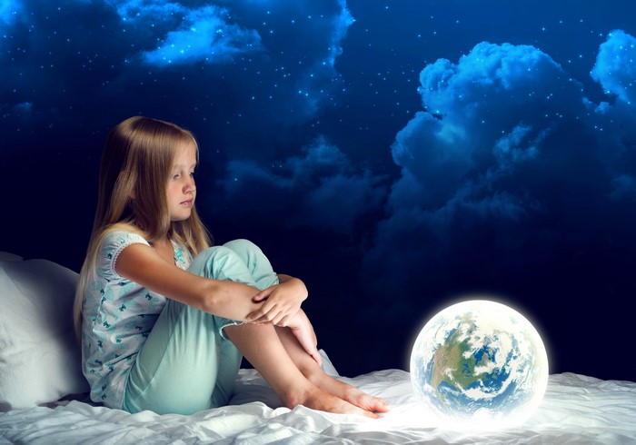 Girl in bed with glowing Earth under starry sky